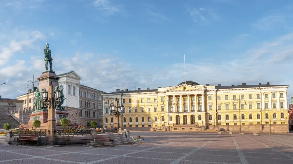 A neoclassical building with columns in an empty square, with a statue of a mounted figure under a clear sky at dawn or dusk.