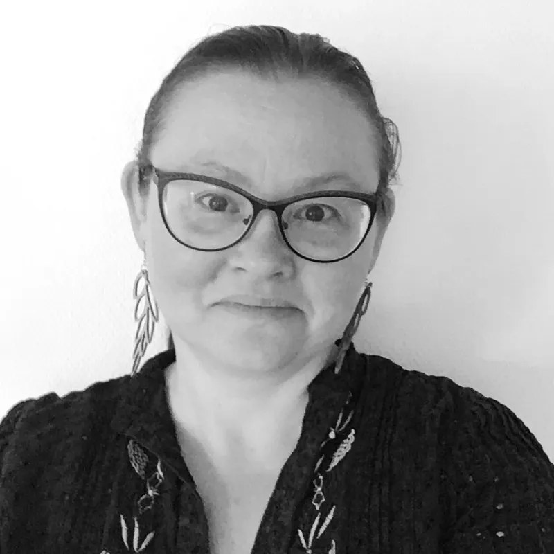 Porträtt av en leende kvinna med glasögon och fjäderörhängen på ett svartvitt foto