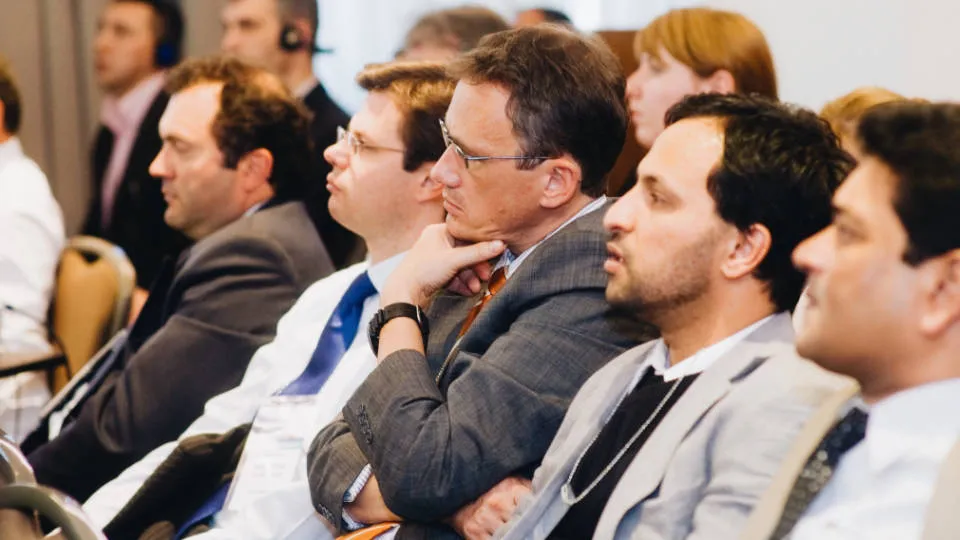 A group of attentive business professionals listening at a conference.