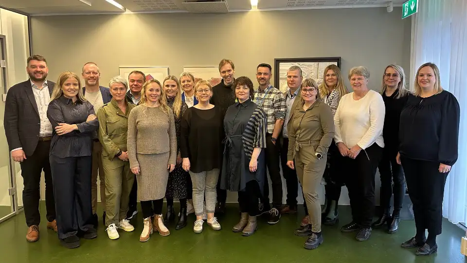 Vi er alle forskjellige og alle like En gruppe mennesker som står sammen i et konferanserom, smilende for et gruppebilde.