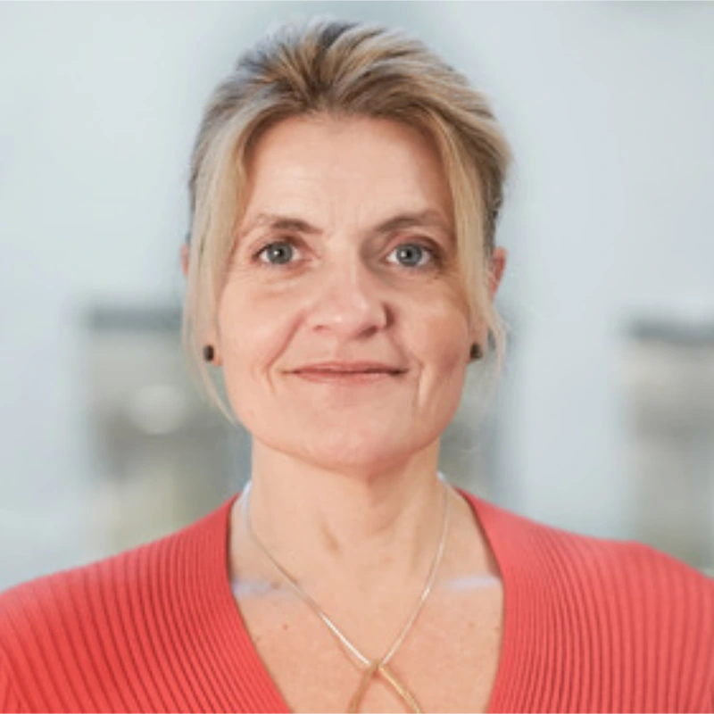 Portræt af en kvinde med lyst hår og rød bluse, der smiler til kameraet.