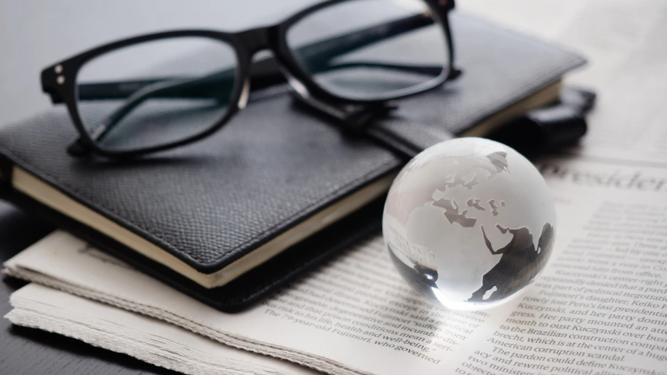 A transparent glass globe with etched outlines of continents, sitting on a newspaper.