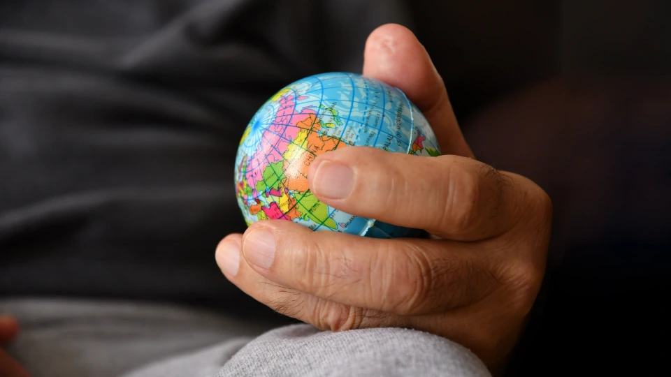 This image depicts a close-up of a hand holding a small globe, symbolizing global connectivity or responsibility. The focus is on the hand and the miniature world map, emphasizing personal interaction with the planet.