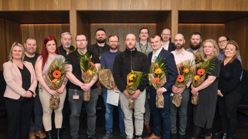 En gruppe mennesker poserer for et bilde i en moderne innendørs setting, flere holder blomsterbuketter og ser fornøyde ut.