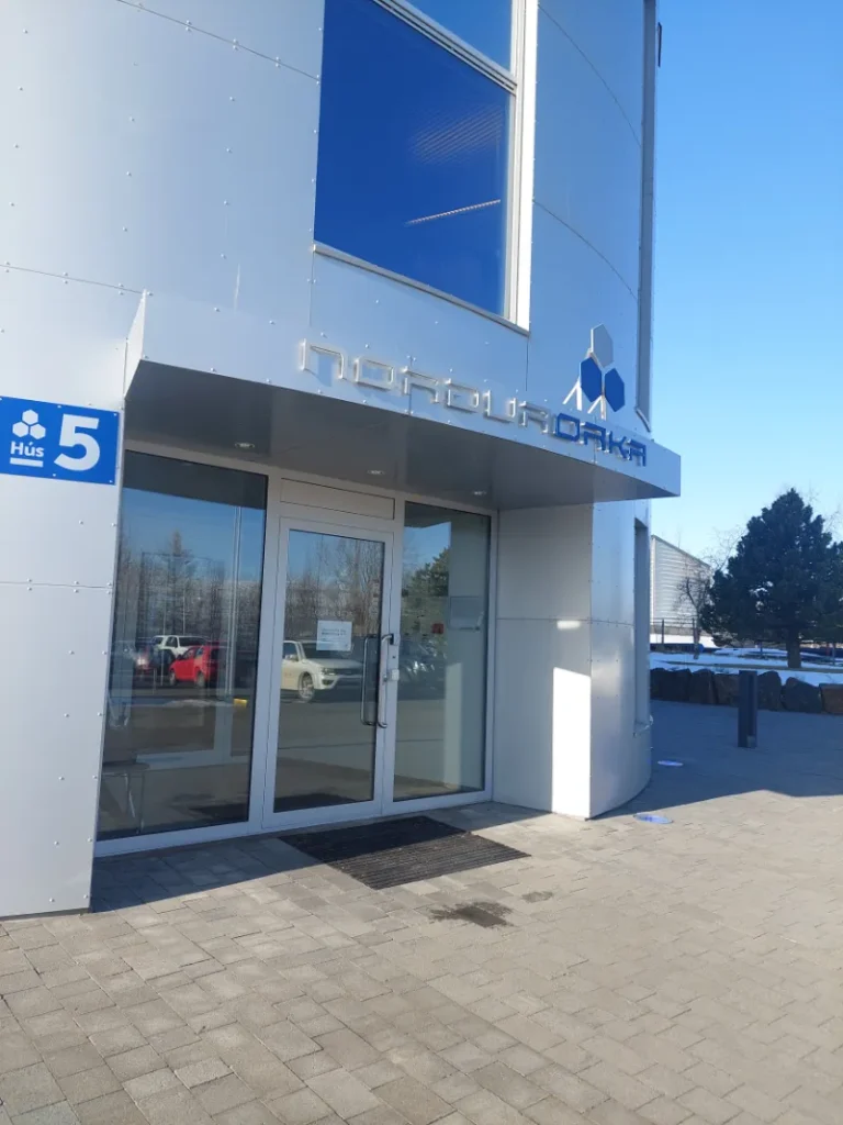 Inngangen til en moderne bygning med skiltet "Norðurorka" og husnummer 5, med speilglassvinduer og en steinbelagt inngang.