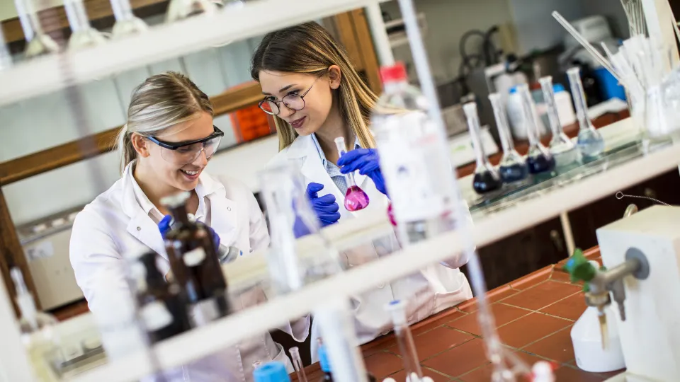 Två unga kvinnliga forskare i laboratorieutrustning arbetar med kemiska lösningar i ett laboratorium.