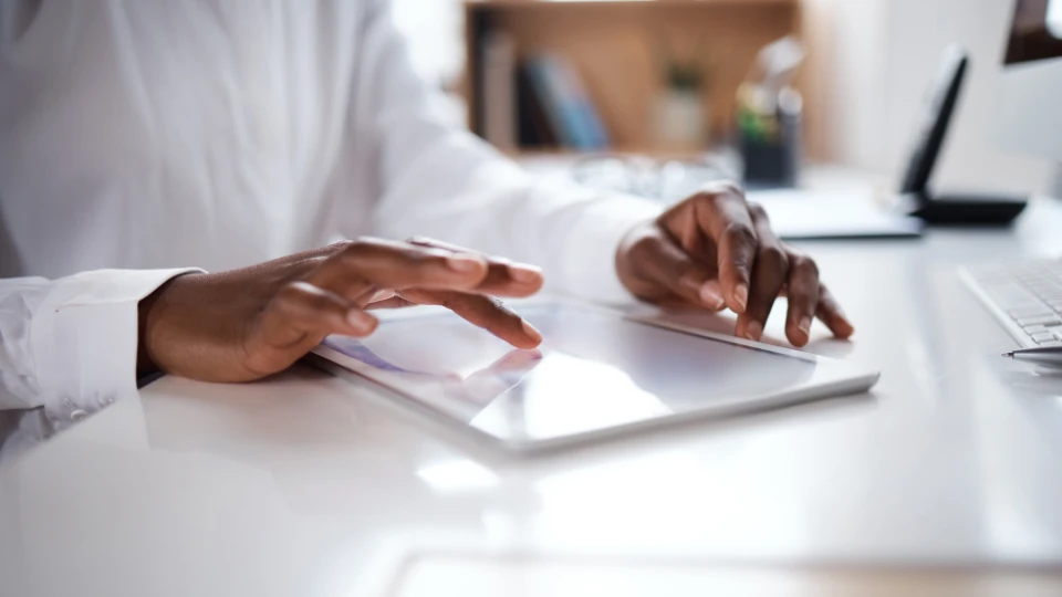 Close-up of a person using a tablet at a white desk in a modern office setting.