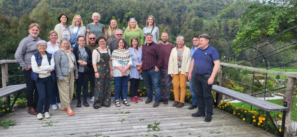 Gruppe mennesker poserer utendørs på en treplattform med skogkledd bakgrunn.