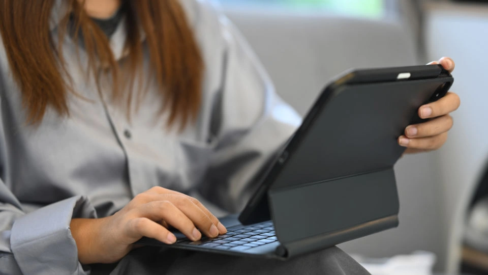 Woman using a tablet with keyboard case while sitting on a couch.