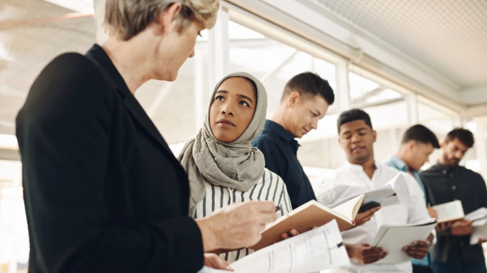 Læring i praksis styrker voksnes posisjon i arbeidslivet Gruppe med studenter og lærer i diskusjon, holder bøker og notater i et moderne undervisningsmiljø.