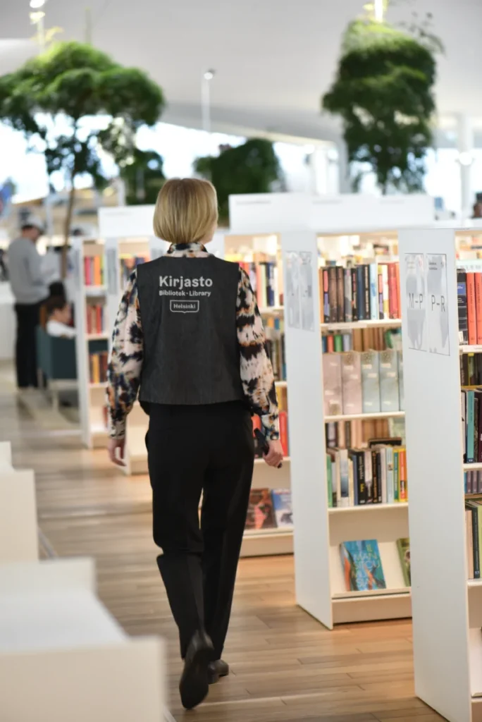 Person i biblioteksväst går bland bokhyllor i Ode i Helsingfors bibliotek.