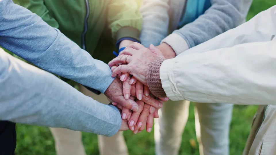 125 millioner kroner for rekruttering av unge i helse En gruppe eldre personer står i en sirkel og legger hendene oppå hverandre i en gest av samhold og fellesskap.