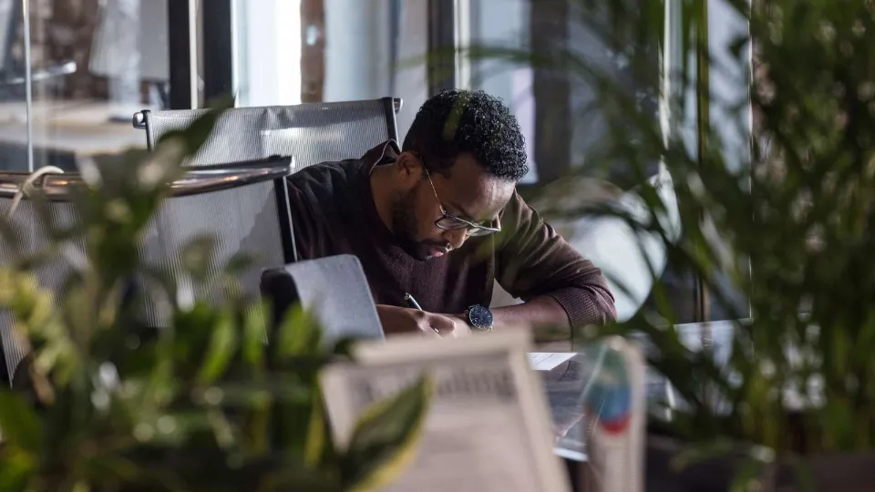 De validerar för att stärka sin konkurrenskraft Man sitter fokuserad vid ett skrivbord och skriver, omgiven av gröna växter i ett modernt kontorsutrymme.