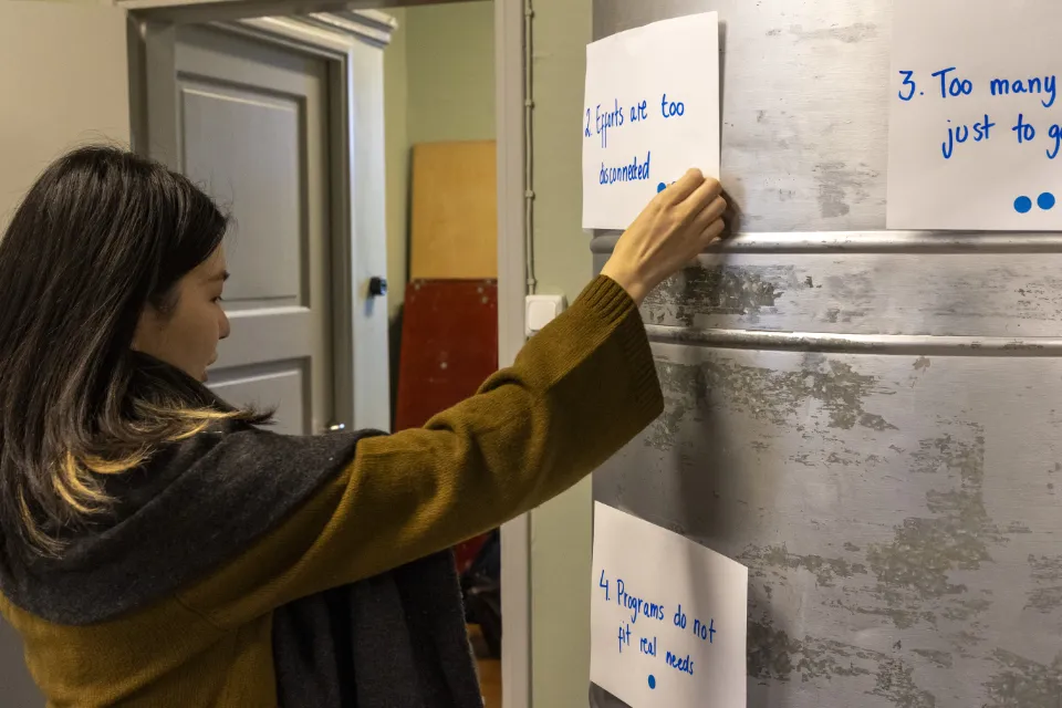 Woman placing handwritten notes on a metallic wall during a workshop or brainstorming session.