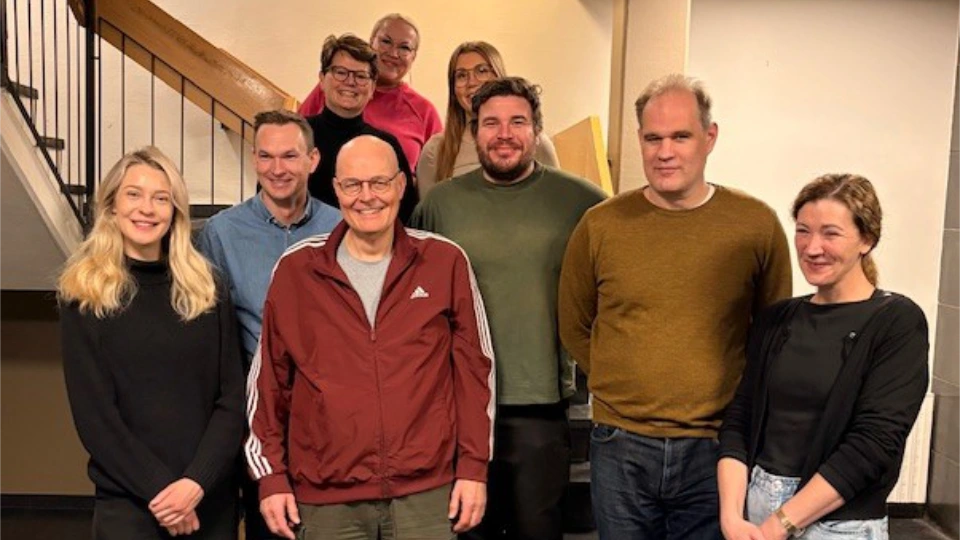 Nordiske arbejdsgruppe for læsefærdigheder i fængsler Gruppebillede af ni smilende voksne foran en trappe i en indendørs opgang, alle iført afslappet hverdagstøj.