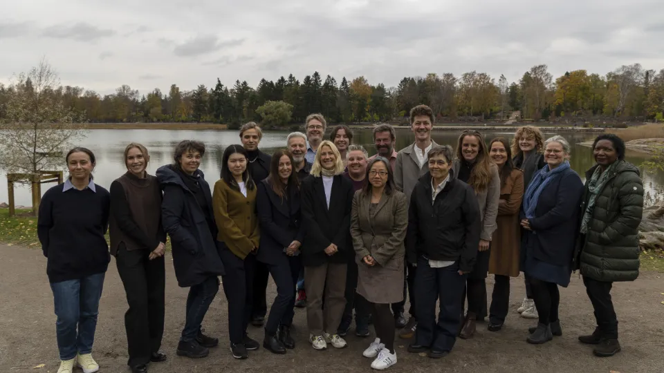 the stakeholder meeting in Helsinki on October 22 Group photo of diverse adults standing outdoors by a lake in autumn, posing together and smiling.