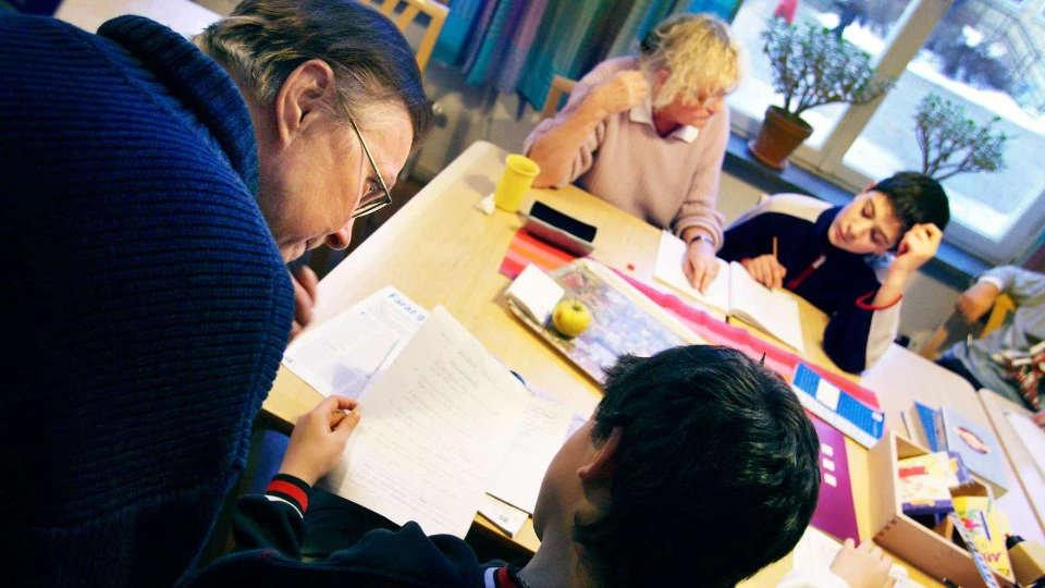 Ny Bildningsbarometer på svenska Lärare och elever arbetar tillsammans vid ett bord med papper, böcker och skolmaterial i ett klassrum.