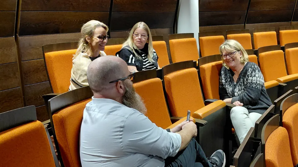 Fyra personer sitter i orange stolar i en hörsal på Åland och diskuterar engagerat i grupp under NEET-seminarium.