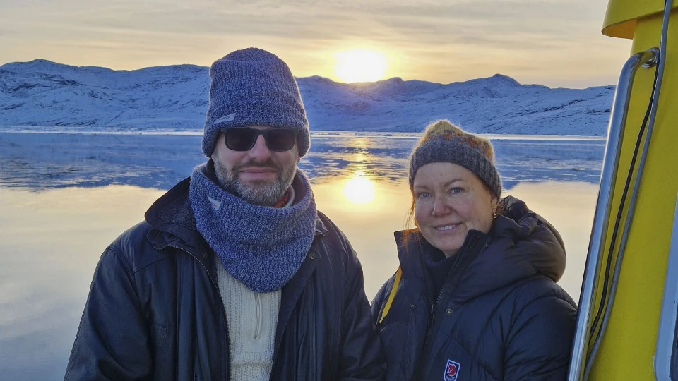 Tristram Hooley og Rie Thomsen Tristram Hooley og Rie Thomsen på en båd i Grønland med sneklædte bjerge og solnedgang i baggrunden.