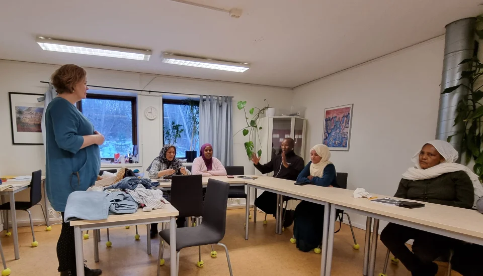 En lärare, Annika, och fem elever i ett klassrum. På katedern ligger tyger. En elev visar med händerna hur stort något är.