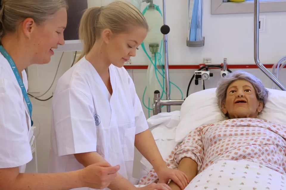 Sykepleiere gir omsorg til en pasientsimulator i en sykehusseng på et treningsrom.