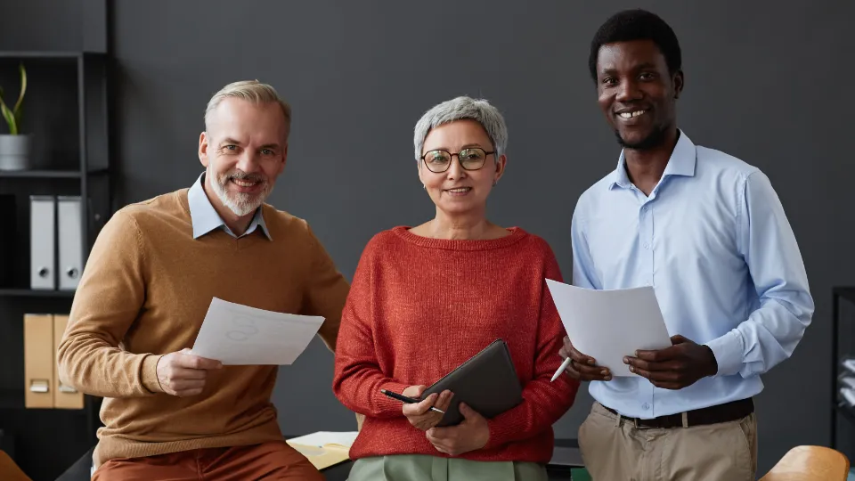 Tre kolleger står i et kontormiljø og holder dokumenter.