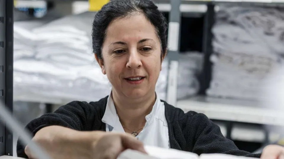 Kvinde sorterer tekstiler eller tøj på hylder i et lager- eller vaskerimiljø.