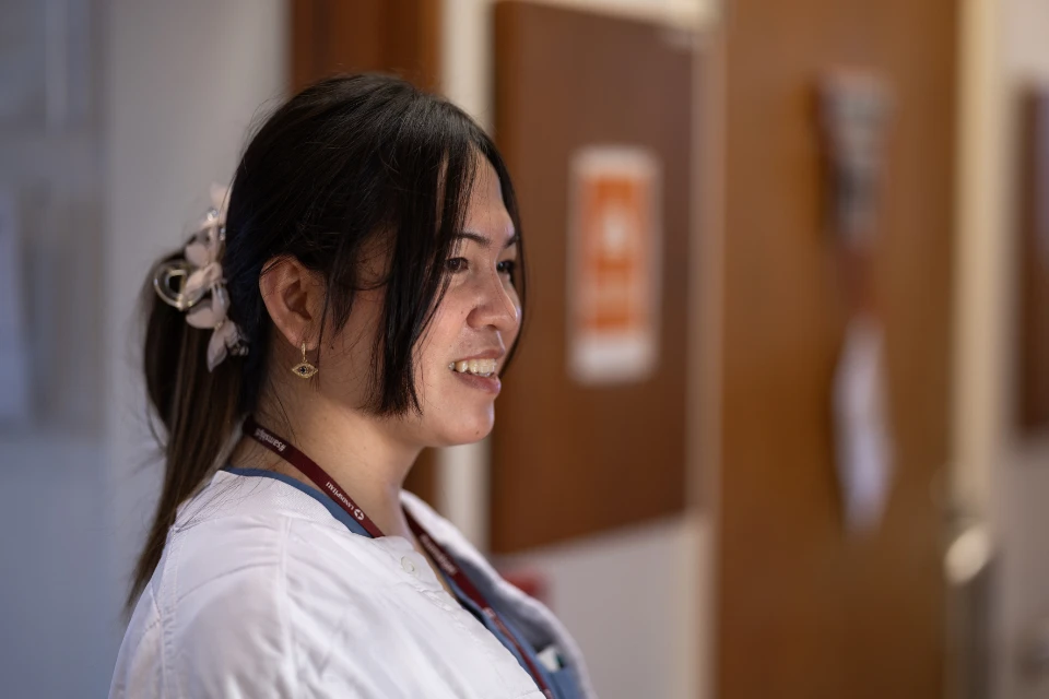 Kvindelig sundhedsarbejder smiler iført hvid kittel og ID-kort på hospital.