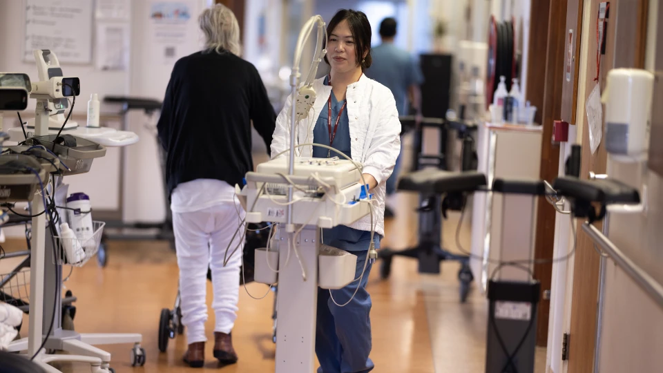 Islandske helsesystem Kvindelig hospitalsansat skubber medicinsk udstyr ned ad hospitalsgang.