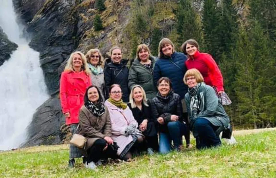 Gruppebilde av kvinner på tur foran en foss og skogkledd fjellandskap.
