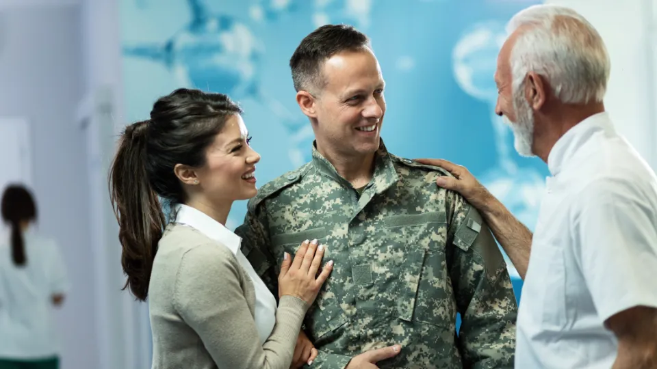 Rekruttering handler om mer lønn – det handler om samfunnsstruktur Smilende soldat i uniform sammen med familie, som snakker i et lyst sykehusmiljø.