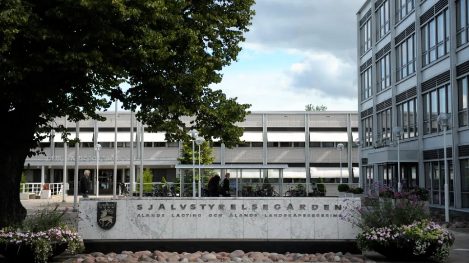 Självstyrelsegården Exteriör av Självstyrelsegården, Ålands landskapsregerings byggnad, med stor stenskylt, blommor och kontorsbyggnader i bakgrunden.