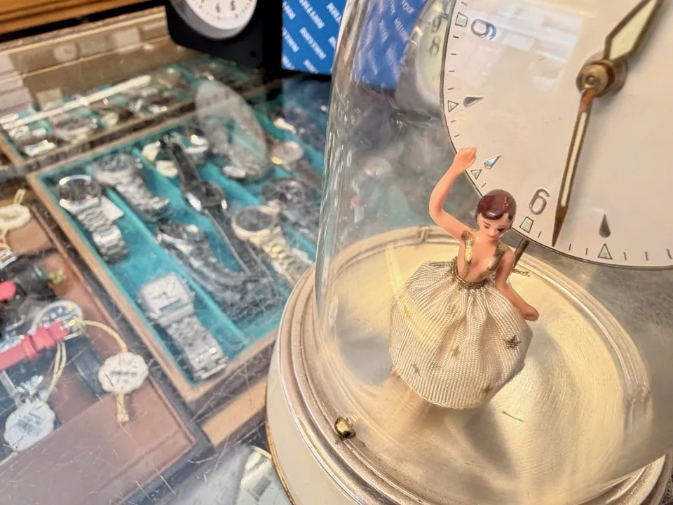 Närbild av dekorativ klocka med liten figur under glaskupa.