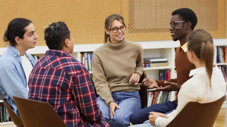 Ge isländskan en chans Fem personer sitter i en cirkel och samtalar i ett bibliotek eller klassrum.
