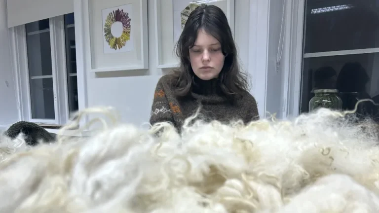 Þorgerður Þorkelsdóttir sitter innendørs og arbeider med lys ull på et bord.