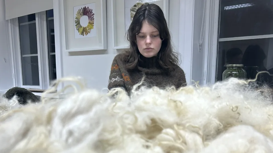 Þorgerður Þorkelsdóttir Þorgerður Þorkelsdóttir sitter innendørs og arbeider med lys ull på et bord.