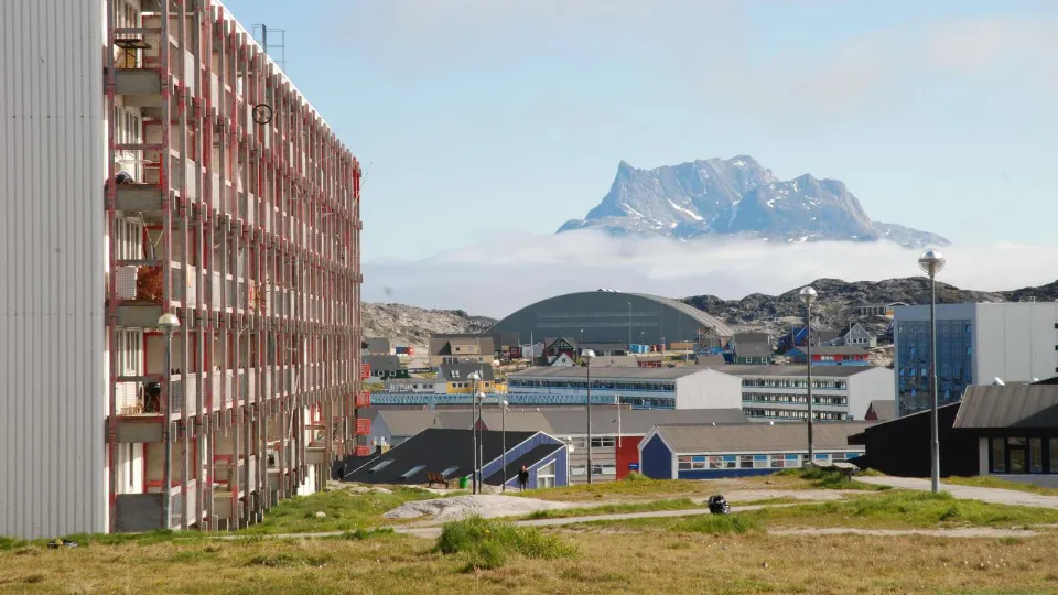 Byområde i Nuuk med boligblokke og farverige bygninger samt et bjerg over tågen i baggrunden.