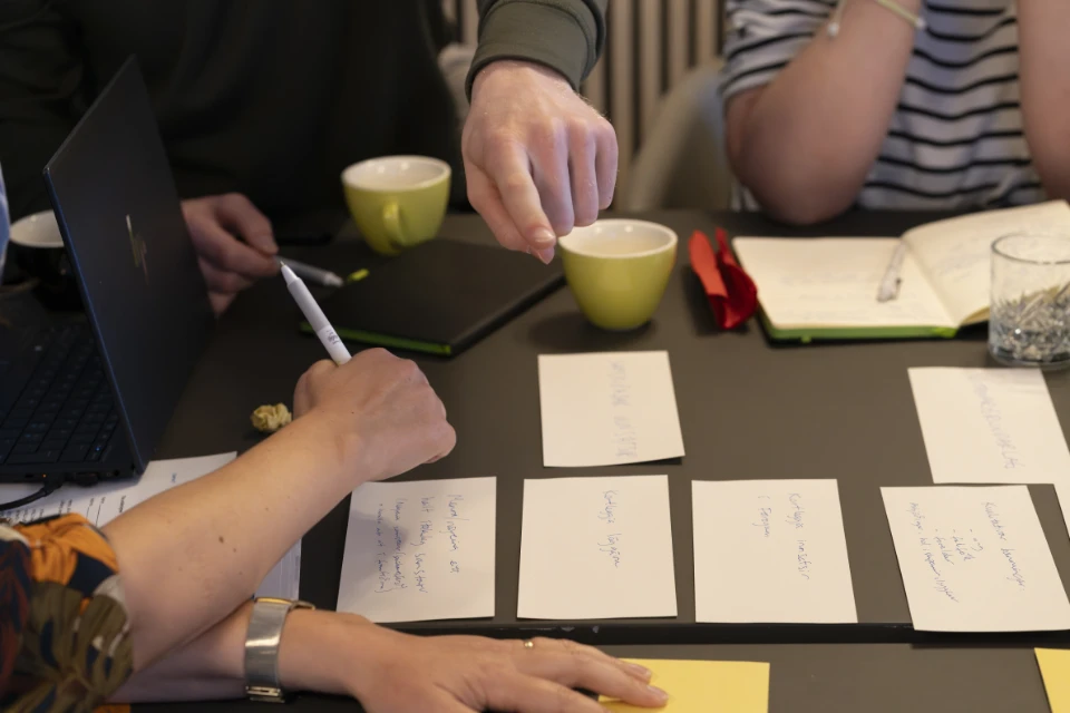 Deltagere arbejder sammen omkring et bord med kort og noter under seminarets workshop.