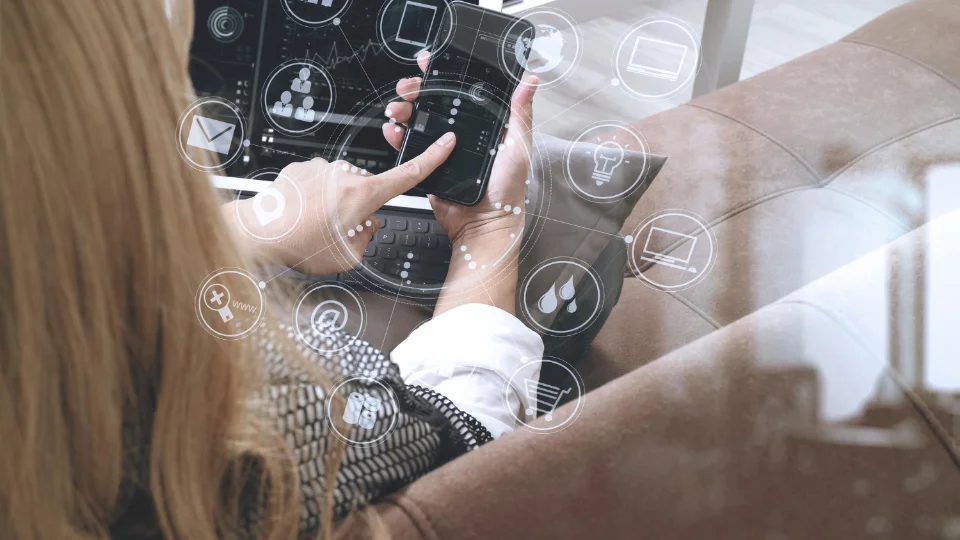 Woman using a smartphone and laptop with digital communication and technology icons overlaid.