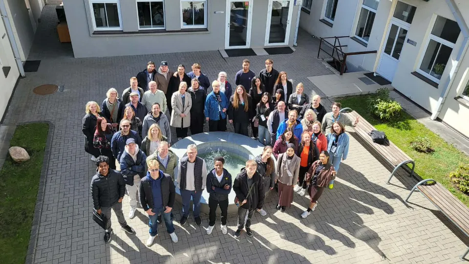 Gruppe af voksenelever og undervisere samlet i en solrig gårdhave omkring et springvand.